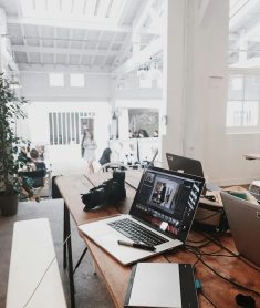 A bright, modern workspace featuring laptops, a camera, and a drawing tablet in an indoor office.